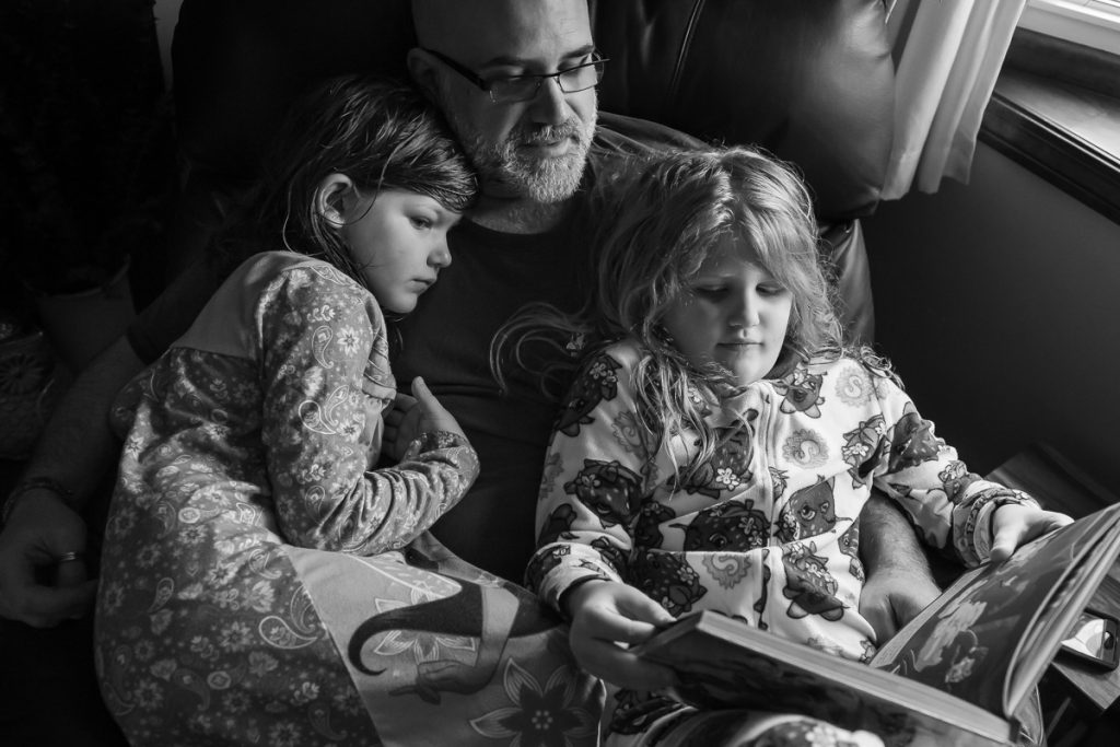 Father and daughters snuggling and reading in chair together