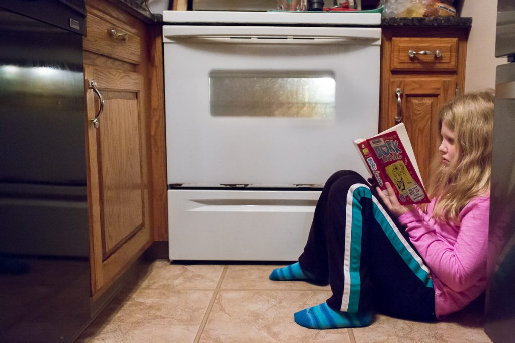A girl reading on the kitchen floor waiting for dinner to be done