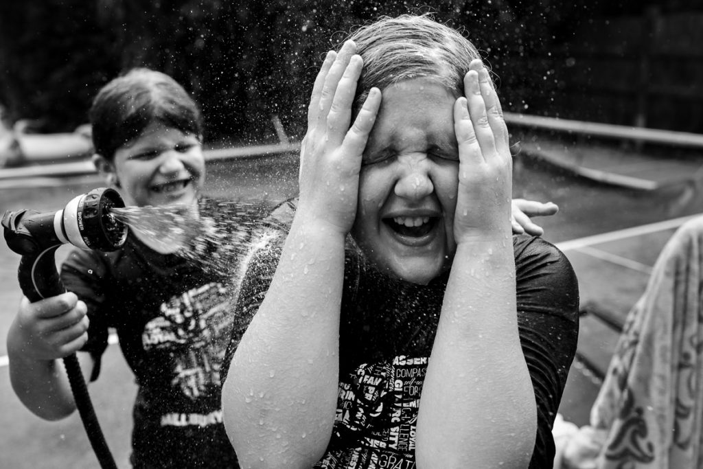 A sister sprays her older sister with the hose